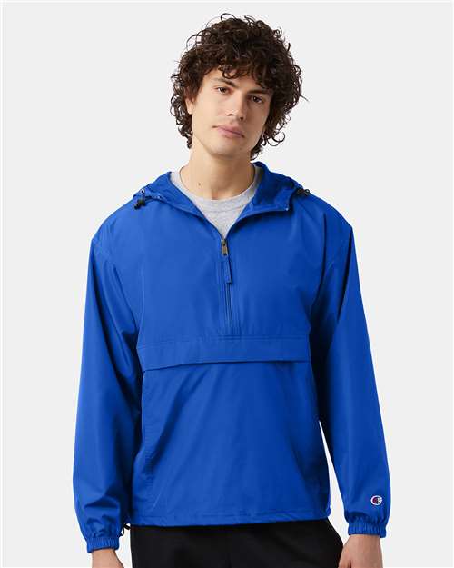 A young man with curly hair wears the Champion CO200 jacket, a bright blue, long-sleeve wind- and water-resistant zip-up with a kangaroo pocket, standing against a plain white background.