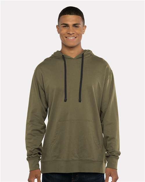 A young man wears the Next Level 9301 olive green cotton-poly hoodie with black drawstrings and a front pocket, smiling against a plain light background—blending comfort with socially conscious manufacturing.