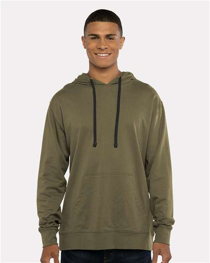 A young man wears the Next Level 9301 olive green cotton-poly hoodie with black drawstrings and a front pocket, smiling against a plain light background—blending comfort with socially conscious manufacturing.