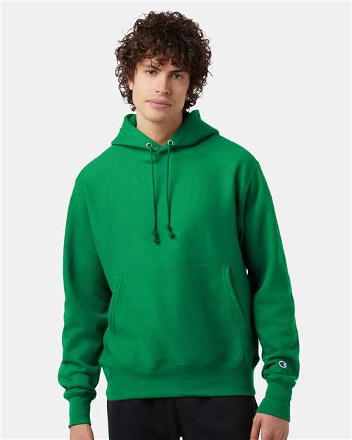A person with curly hair faces forward against a plain light background, wearing a bright green Champion S101 hoodie featuring drawstrings and a front pocket.