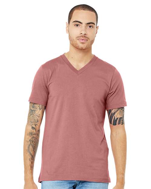 A person with short hair and tattooed arms is wearing a mauve BELLA + CANVAS 3005 unisex V-neck Airlume combed cotton T-shirt and light blue jeans, standing against a plain white background.