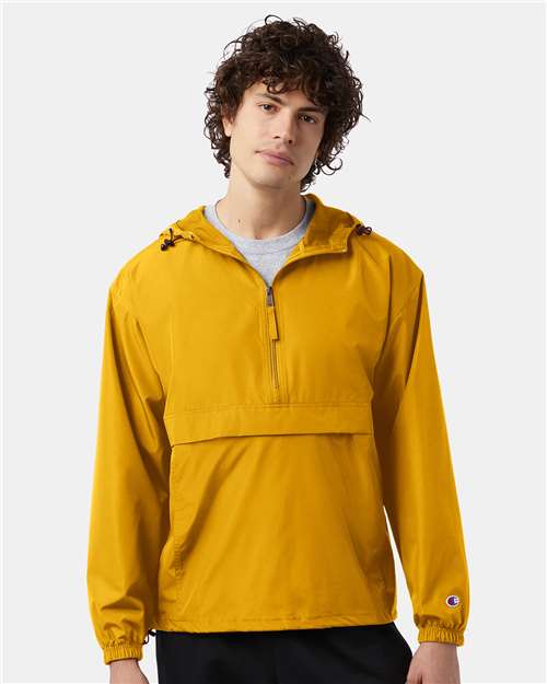 A person with curly hair wears the Champion CO200 bright yellow wind- and water-resistant jacket, featuring a front zipper and large pocket, standing against a plain light background.