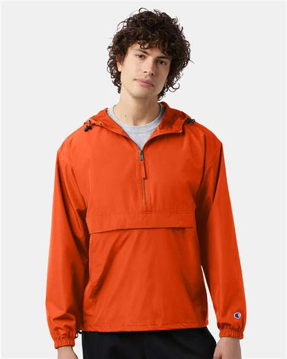 A young man with curly hair wears the Champion CO200 micro poplin pullover hooded jacket in orange, featuring a front zipper and flap pocket, standing against a plain light background.