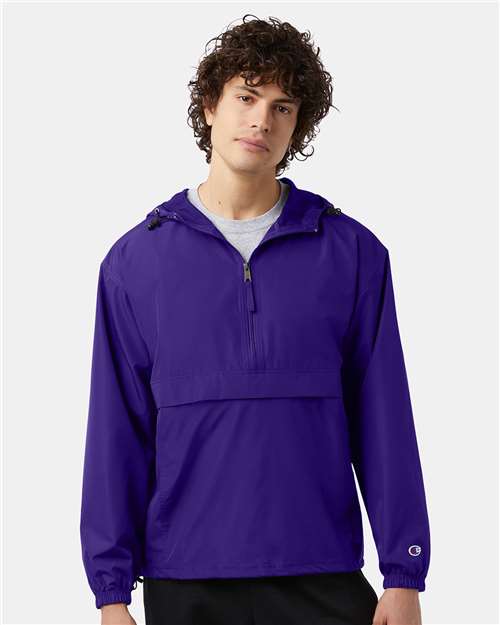 A person with curly brown hair is wearing a purple Champion CO200 micro poplin wind- and water-resistant jacket with a front zip and flap pocket, standing against a plain light background.