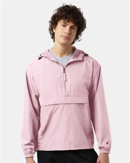 A young man with curly brown hair wears the Champion CO200 light pink hooded micro poplin wind- and water-resistant jacket over a gray shirt, standing against a plain light background.