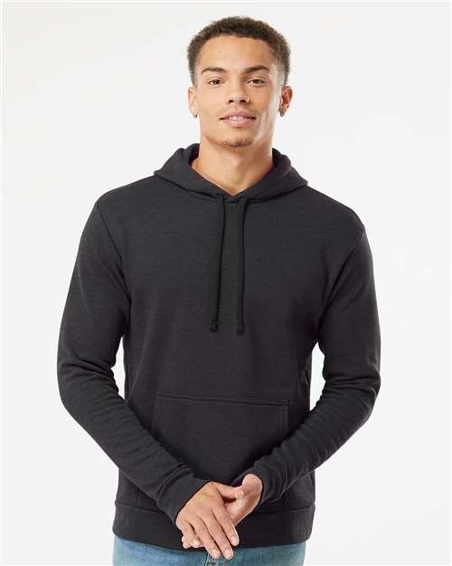 A young man stands facing the camera against a white background, wearing the Next Level 9302 black hooded sweatshirt made of soft cotton polyester fleece with a front pocket and drawstrings.
