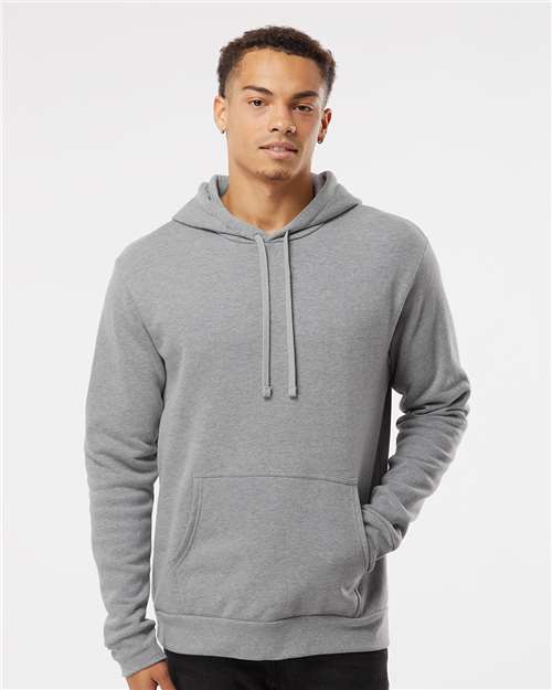 A young man wears the Next Level 9302 hoodie, crafted from soft cotton-polyester fleece with a front pocket and drawstrings, standing against a white background and looking at the camera with a relaxed expression.