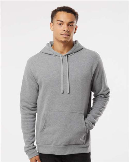 A young man wears the Next Level 9302 hoodie, crafted from soft cotton-polyester fleece with a front pocket and drawstrings, standing against a white background and looking at the camera with a relaxed expression.