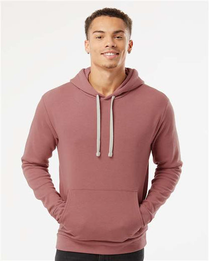 A young man smiles in a Next Level 9303 mauve cotton-polyester hoodie with a jersey-lined hood and front pocket, standing against a plain white background.