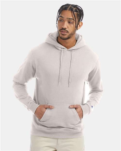 A man with braided hair wears a light gray Champion S700 hoodie, made from recycled polyester, hands in the front pocket, standing against a plain light background.
