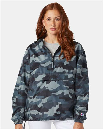 A woman with long red hair wears the Champion CO200 blue and gray camouflage wind- and water-resistant jacket with a front zipper and hood, standing against a plain light background.