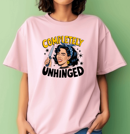 A woman wears DB Custom Creations Unhinged pink T-shirt, featuring a cartoon retro-style woman with a knife, star accents, and Completely Unhinged in bold yellow and black. Durable DTF printing ensures vibrant, lasting color.