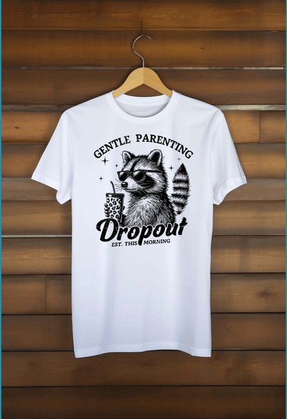 A white DB Custom Creations T-shirt, Gentle Parenting Drop Out, features DTF printing of a raccoon with sunglasses holding a coffee cup and the text “Gentle Parenting Dropout Est. This Morning.”.