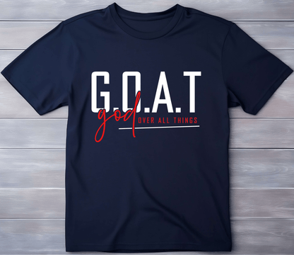 DB Custom Creations’ G.O.A.T navy blue t-shirt features G.O.A.T in bold white, god over all things below, and god in red script—created using premium DTF transfer and displayed flat on a wooden surface.