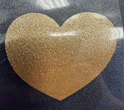 A large, glittery gold heart shape is centered on a dark background with reflections of overhead lights on its surface—perfect for creating eye-catching T-shirts or apparel using DB Custom Creations’ Custom Puff Transfers for T-Shirts and Apparel.