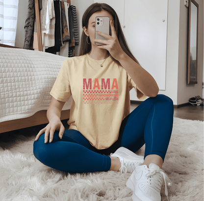A woman sits cross-legged on the floor, taking a mirror selfie while wearing DB Custom Creations Hardworking Mama yellow shirt with bold DTF print and blue leggings; a bed and clothes appear in the background.