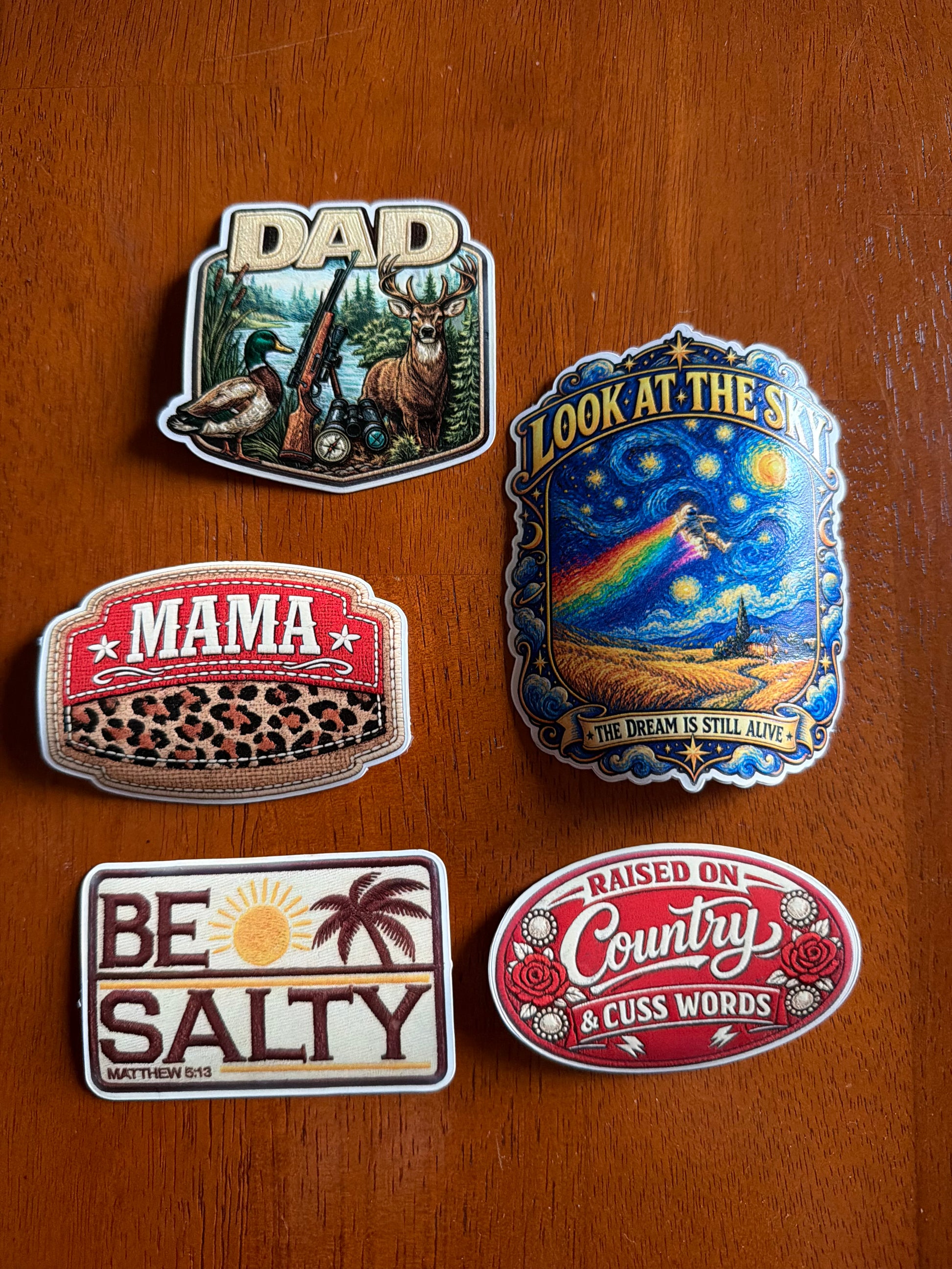 Five colorful TPU Full Color Patches by DB Custom Creations featuring illustrations and text: DAD with wildlife, MAMA with leopard print, LOOK AT THE SKY, BE SALTY, and RAISED ON COUNTRY & CUSS WORDS.