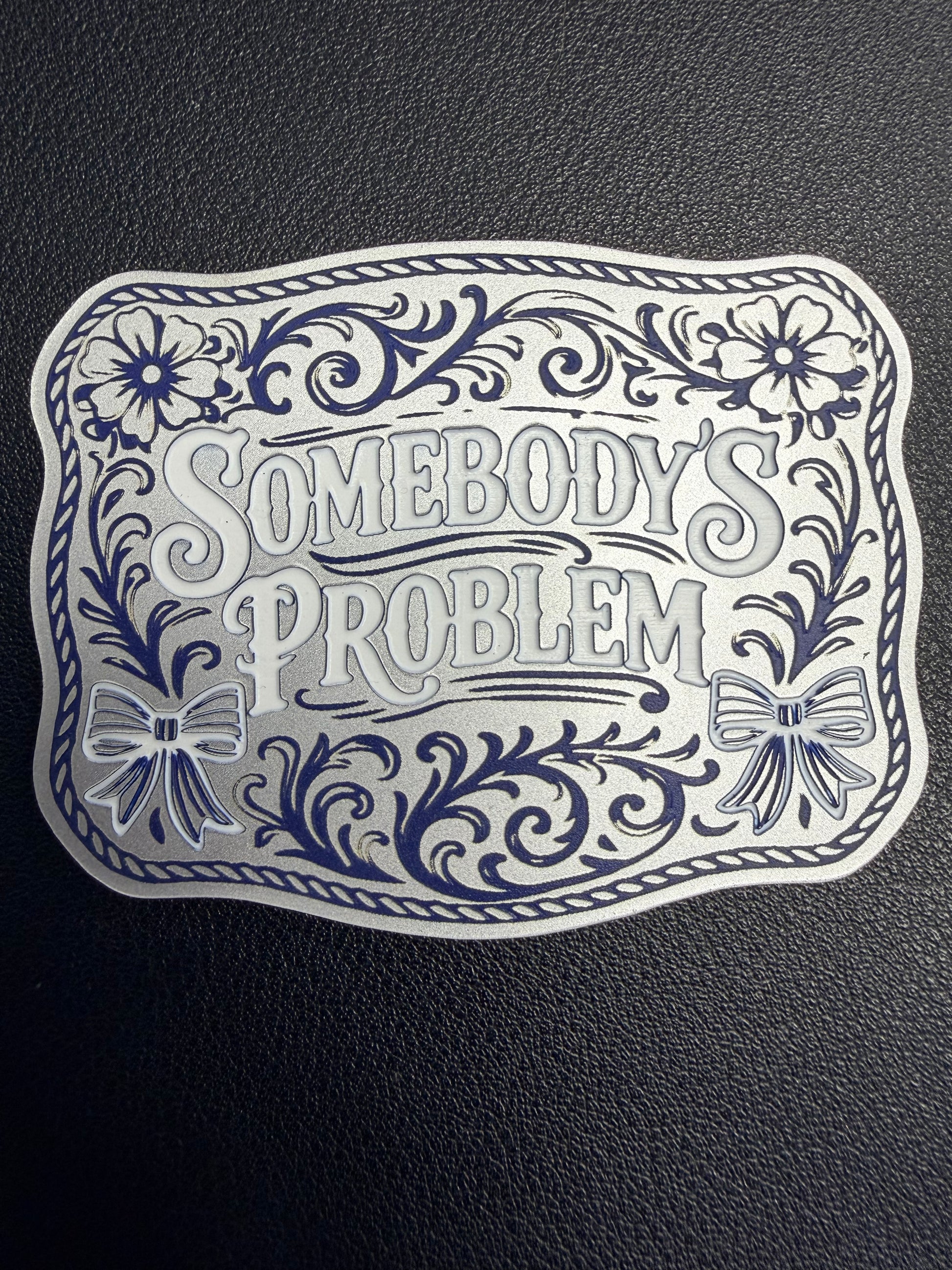 DB Custom Creations' custom laser engraved tri layered acrylic patches for hats showcase bold floral designs, bows, ornate borders, and the phrase "Somebody’s Problem," set on a textured black base with strong adhesive for secure use.