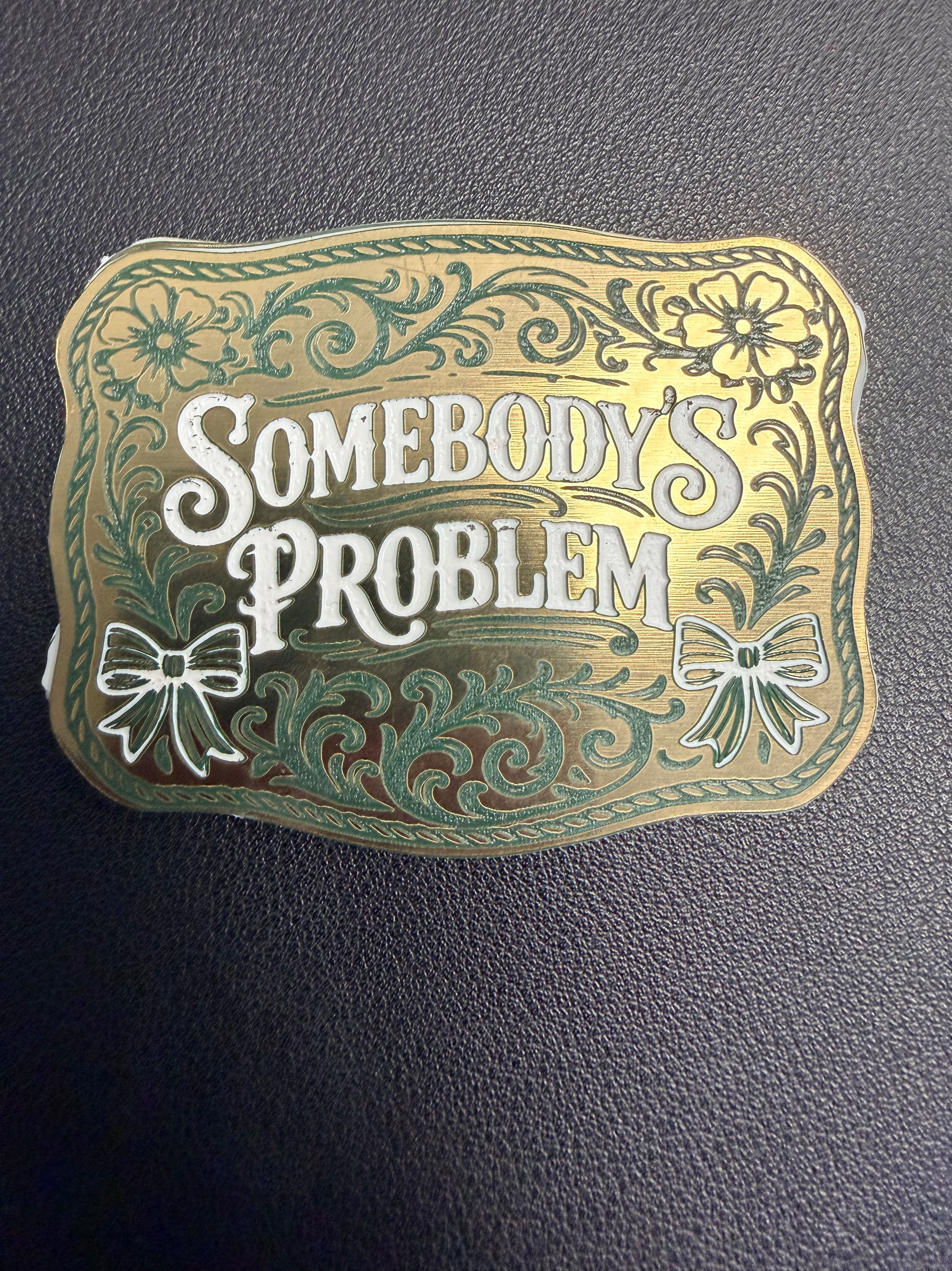 DB Custom Creations' Custom Laser Engraved Tri Layered Acrylic Patch for Hats features bold white "Somebodys Problem" text with gold and green floral and bow designs, resembling a high-quality plaque on a textured dark background.