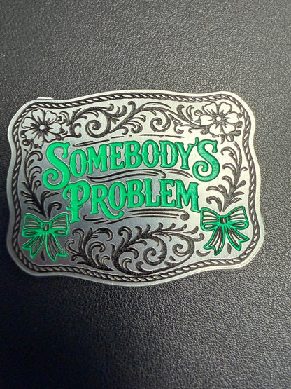 The Custom Laser Engraved Tri Layered Acrylic Patch for Hats by DB Custom Creations features bold green "Somebodys Problem" text with silver, green floral designs, and bows that pop against a dark textured background.