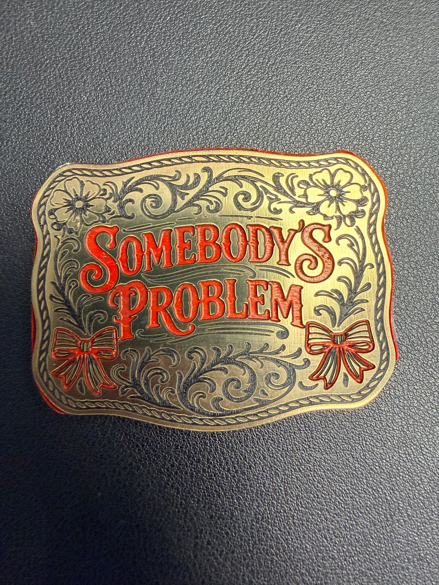 DB Custom Creations presents Custom Laser Engraved Tri Layered Acrylic Patches for hats—ornate floral and bow details with "Somebodys Problem" in bold red on textured gray, crafted with high-quality techniques for a lasting impression.