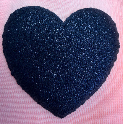 A textured, dark blue heart created with DB Custom Creations' Custom Puff Transfers for T-Shirts and Apparel rests on a pink, ribbed fabric background, showcasing the trendy style popular in modern fashion.