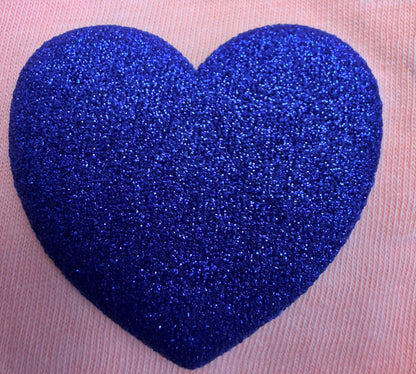 A glittery, textured blue heart stands out against a soft pink fabric background, making it an ideal design for customizing T-shirts or other apparel with DB Custom Creations’ Custom Puff Transfers for T-Shirts and Apparel.