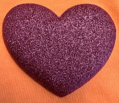 A glittery purple heart shape rests on an orange textured background, perfectly capturing the playful spirit featured in DB Custom Creations' Custom Puff Transfers for T-Shirts and Apparel.
