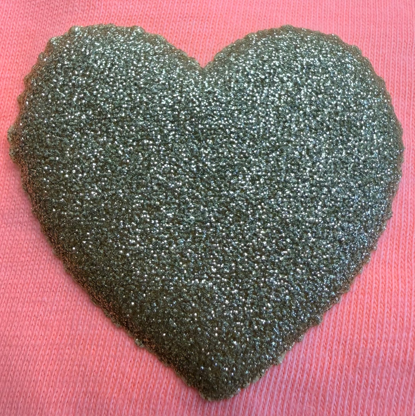 A glittery, textured silver heart design is featured on a pink fabric background, making it an ideal choice for enhancing T-Shirts and apparel with DB Custom Creations' Custom Puff Transfers.