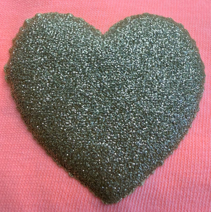 A glittery, textured silver heart design is featured on a pink fabric background, making it an ideal choice for enhancing T-Shirts and apparel with DB Custom Creations' Custom Puff Transfers.