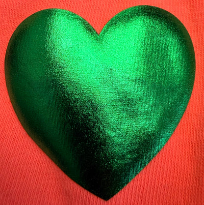 A shiny, metallic green heart shape rests on a textured, bright pink background—ideal for creating bold looks on T-Shirts or other apparel using Custom Puff Transfers for T-Shirts and Apparel from DB Custom Creations.