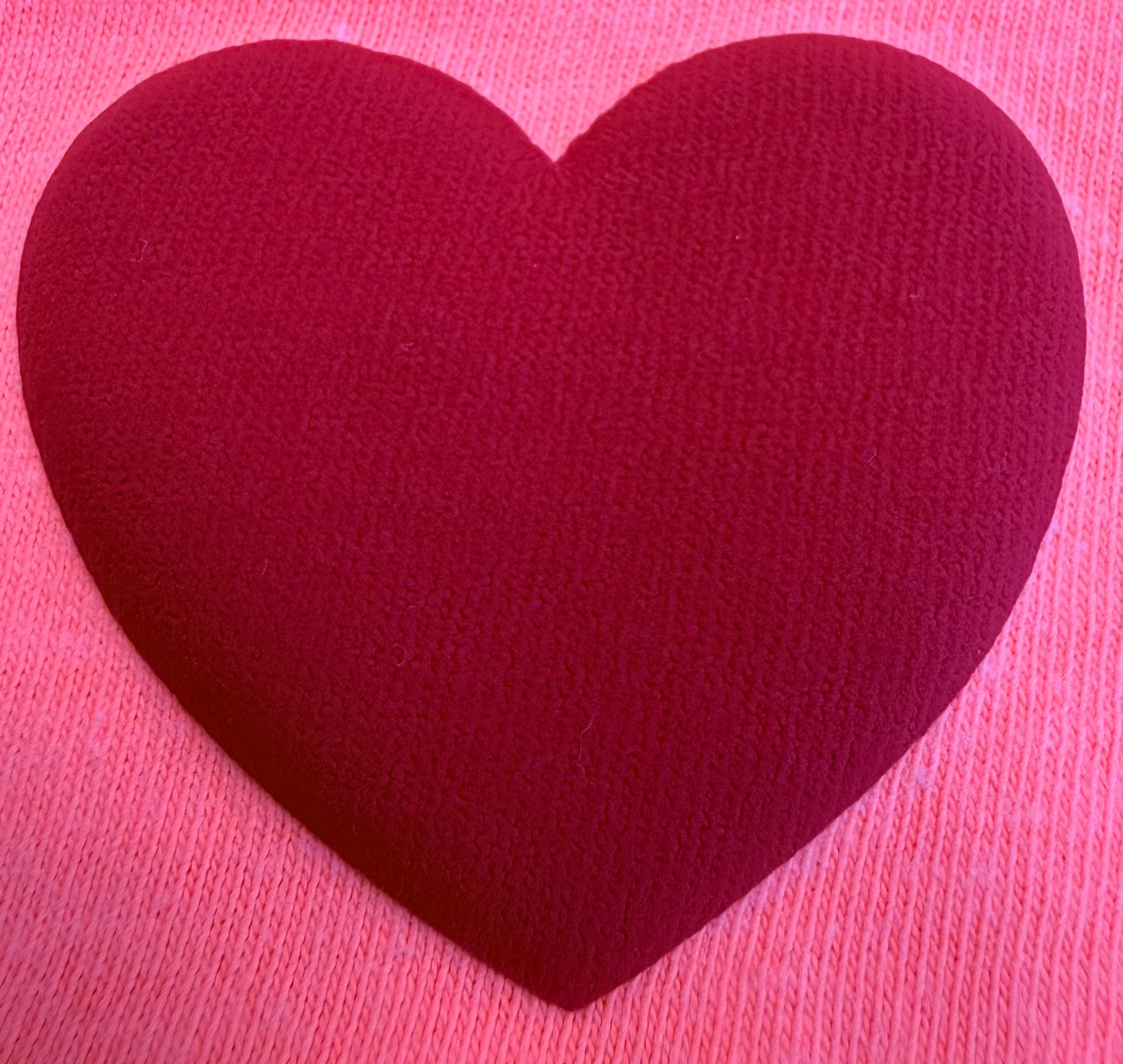 A large, textured red heart sits centered on a soft pink knitted fabric background, capturing the cozy charm featured in DB Custom Creations' Custom Puff Transfers for T-Shirts and Apparel.