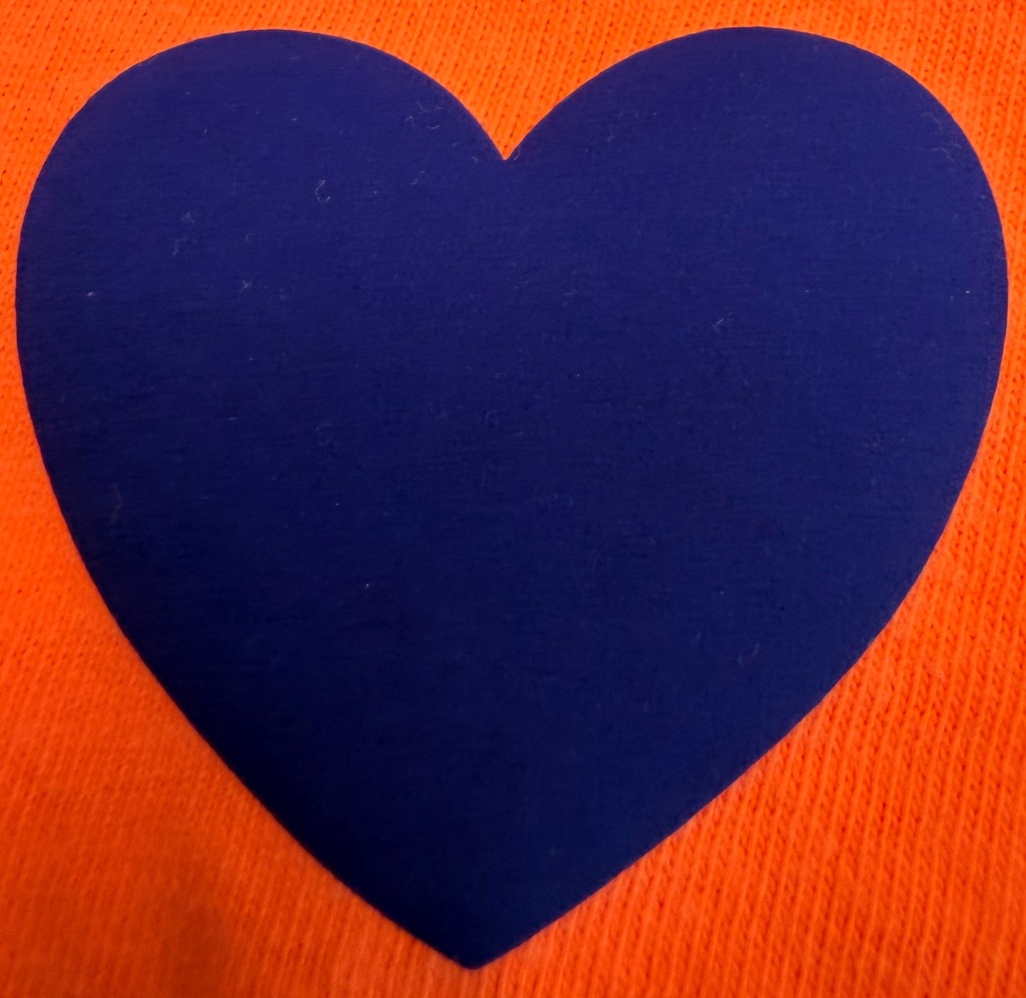 A striking design for t-shirts and apparel from DB Custom Creations’ Custom Puff Transfers features a large, solid blue heart centered on an orange textured background.