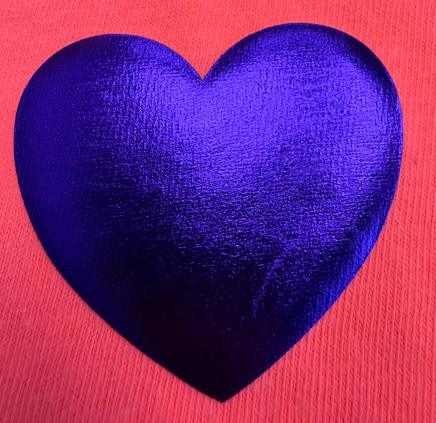 A glossy, dark blue heart rests on a textured, vibrant pink background—an attention-grabbing design ideal for T-shirts or other apparel using DB Custom Creations’ Custom Puff Transfers.