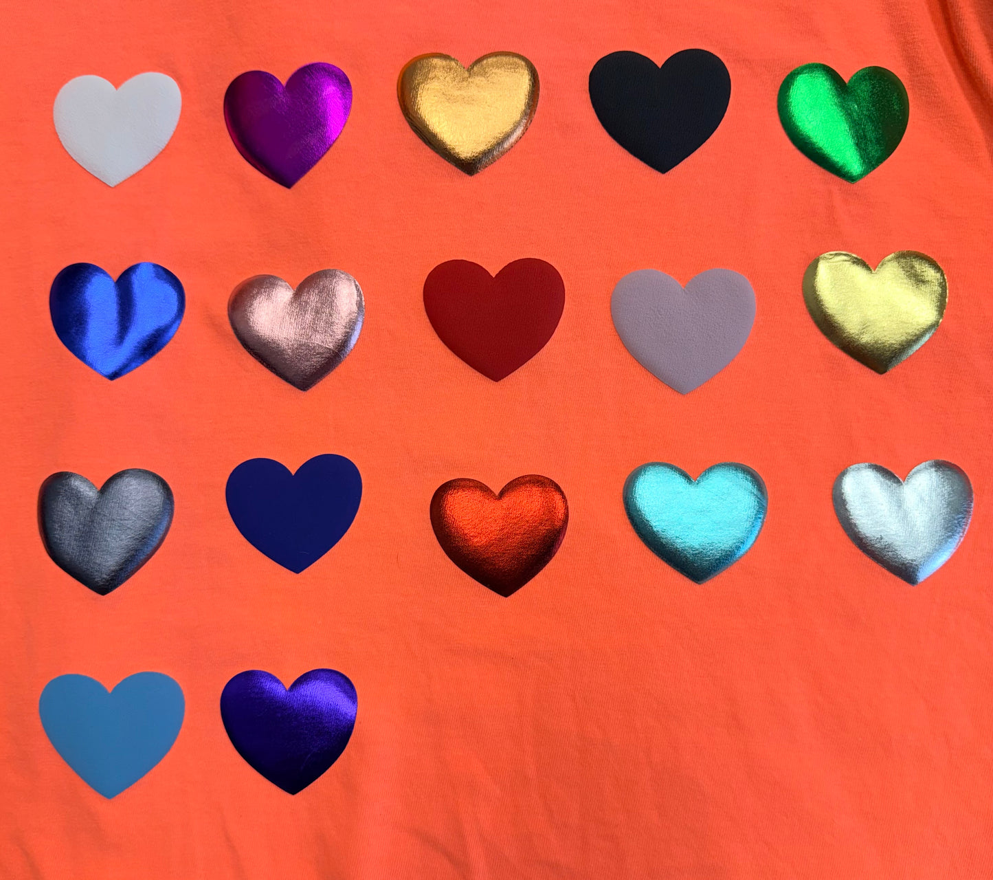 Fifteen hearts in a mix of metallic and matte colors are arranged in a grid on a vivid orange background—perfect for bringing bold style to your T-shirts or apparel with Custom Puff Transfers for T-Shirts and Apparel from DB Custom Creations.