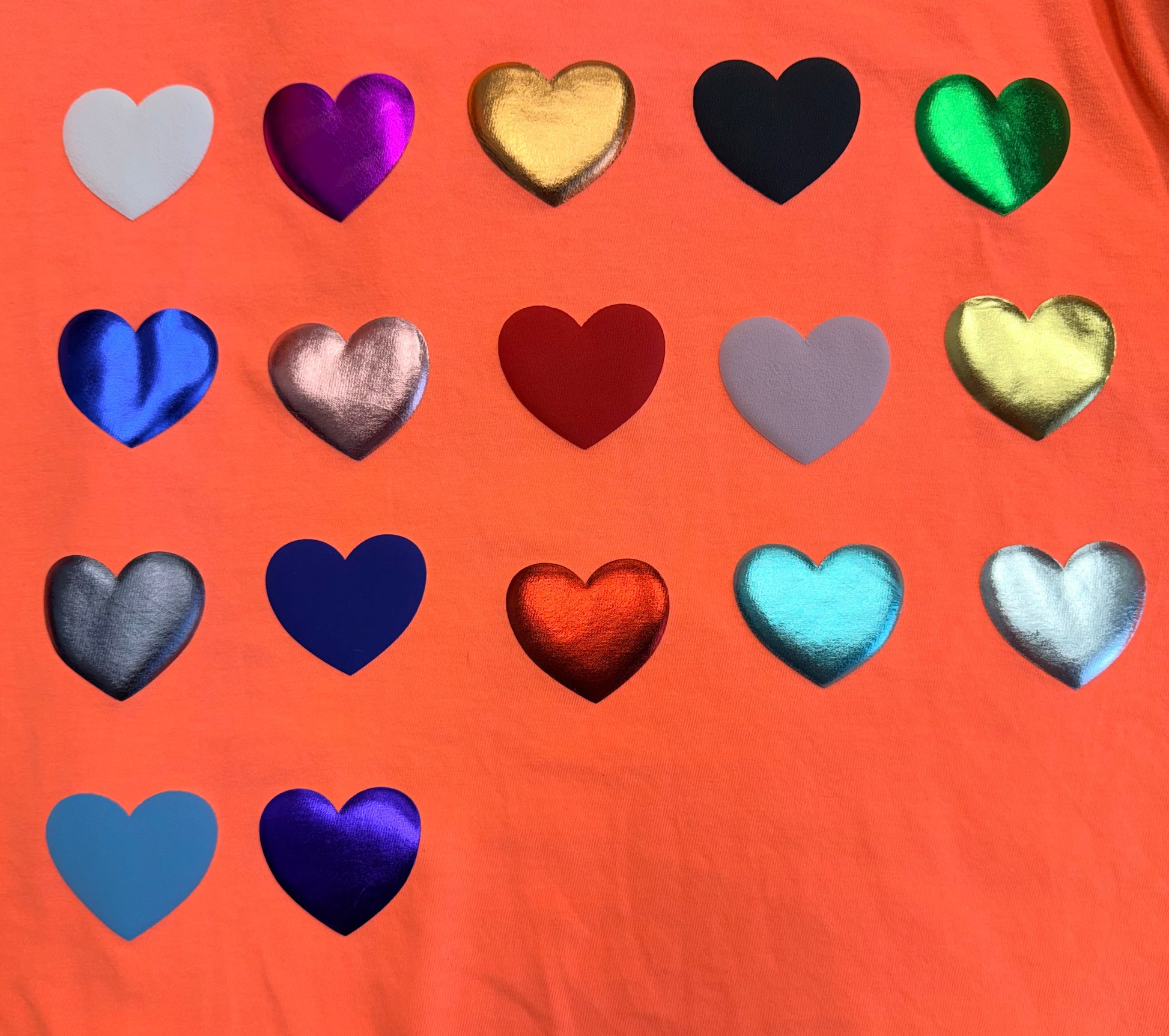Fifteen hearts in a mix of metallic and matte colors are arranged in a grid on a vivid orange background—perfect for bringing bold style to your T-shirts or apparel with Custom Puff Transfers for T-Shirts and Apparel from DB Custom Creations.