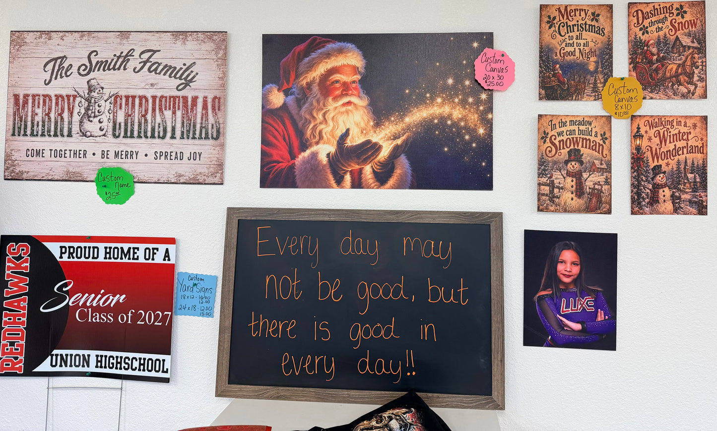 A wall display featuring DB Custom Creations Canvas Panel Printing with Christmas themes, a high school graduation sign, a framed chalkboard quote, and a portrait of a young girl in a gymnastics uniform.