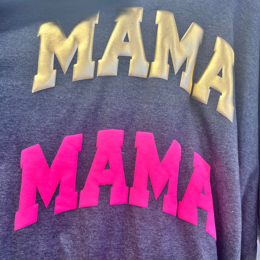 The Puff Transfers T-shirt by DB Custom Creations features MAMA printed twice—gold on top, bright pink below—on a dark gray shirt, adding a bold and playful touch to your wardrobe.