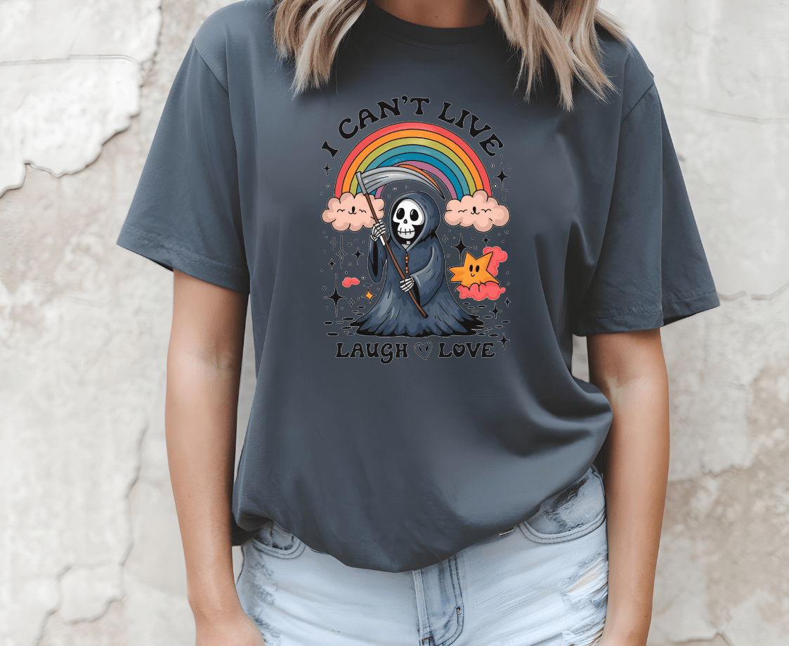 A woman wears a dark gray DB Custom Creations t-shirt called I cant live laugh love, featuring a colorful cartoon grim reaper, rainbow, clouds, and the text “I CAN’T LIVE LAUGH LOVE.”.