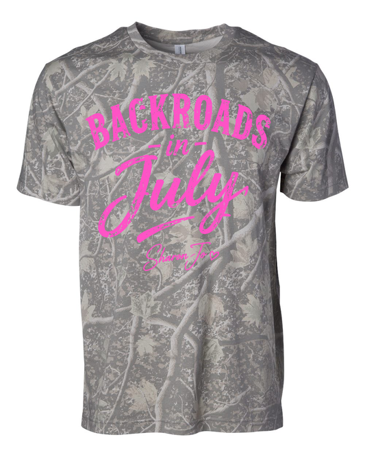 The Camo Pink Back Roads T-shirt by DB Custom Creations features a gray camo pattern with "Backroads in July" in large bright pink script and smaller pink "Shane Joe" text beneath it.