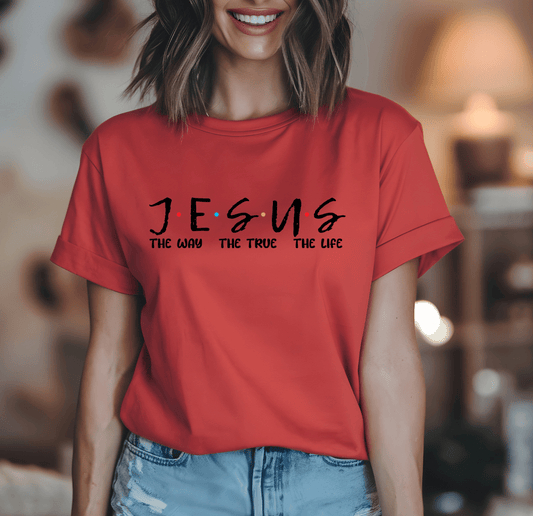 A woman wears a red Jesus t-shirt by DB Custom Creations, featuring bold black text The Way The True The Life with 11-inch DTF printing, standing indoors against a blurred background.