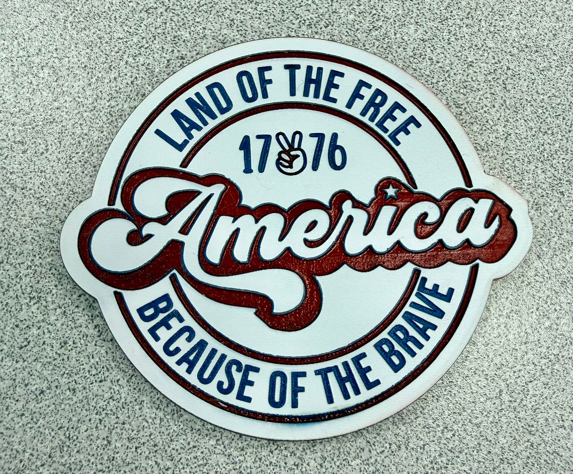 The Land of the Free sticker by DB Custom Creations features "America" in bold, "1776" with a peace hand sign, and reads "Land of the Free Because of the Brave" on a speckled gray background—great with premium patches.