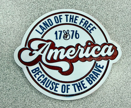 The Land of the Free sticker by DB Custom Creations features "America" in bold, "1776" with a peace hand sign, and reads "Land of the Free Because of the Brave" on a speckled gray background—great with premium patches.