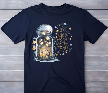 The “Let your light Bloom” navy tee by DB Custom Creations features an 11 DTF print of a glowing firefly and flower jar, with “Let your light bloom” in yellow script, surrounded by stars and flowers.