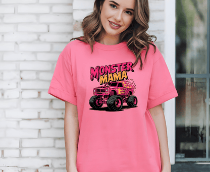 A smiling woman wears the Monster mama T-shirt by DB Custom Creations, featuring a cartoon monster truck and Monster Mama in bold graffiti-style text, printed with vibrant DTF printing. She stands before a white brick wall.