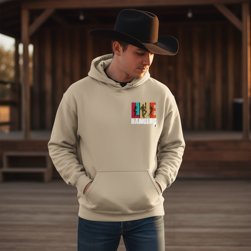 A man wearing a black cowboy hat and a Gildan Sand Hoodie 18500 by DB Custom Creations stands outdoors on a wooden deck, hands in his pockets, with a lit wooden building in the background.