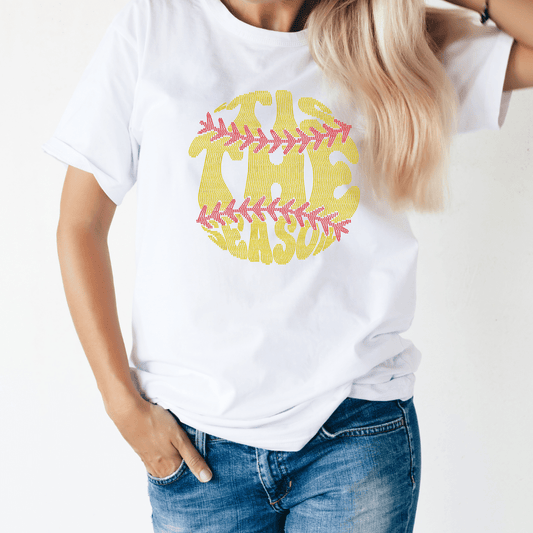 A person with long blonde hair and one hand in their pocket wears a white T-shirt featuring DB Custom Creations 10 x 10.5 Spangle Transfer - Softball Season design, paired with blue jeans.