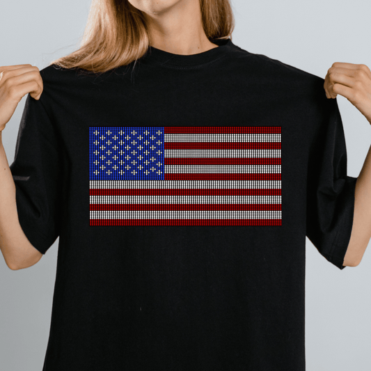A person displays the sides of a black T-shirt decorated with DB Custom Creations Spangle Transfer - US Flag (10 x 5.5) rhinestone design. Only the lower half of their face is visible against a plain light gray background.