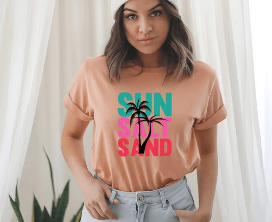 A woman wears the DB Custom Creations sun salt sand peach t-shirt, featuring bold text and a palm tree graphic made with DTF printing, standing indoors with hands in her pockets, white curtains and a plant behind her.
