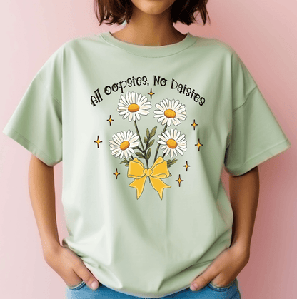A person wears the All Oopsie No Daisies t-shirt by DB Custom Creations, featuring a DTF transfer of daisies tied with a yellow bow and the text above them, all on a light green tee with a light pink background.